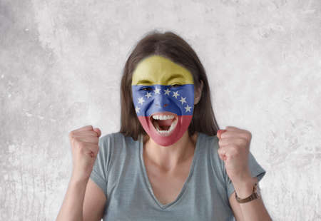 Young woman with painted flag of Venezuela and open mouth looking energetic with fists upの写真素材