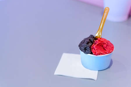 Small blue cup of dark chocholate  and raspberry ice cream in shop on a blue tableの写真素材