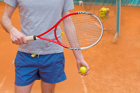 Tennis player holding racket and yellow ball on the orange tennis courtの写真素材