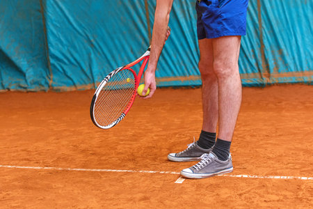 Tennis player holding racket and yellow ball ready to serve on the tennis court