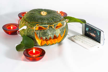 A bright pumpkin head, with glasses and earphones takes a selfie with the phone. Isolated, white background.の写真素材
