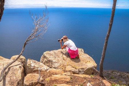Nature travel photographer woman taking pictures on a spectacular cliff during the trekking Fluted Cape Within the South Bruny National Park Bruny Island, Tasmania Australia.の写真素材