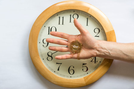 Hourglass of time hold by an hand on top of a clock, white .