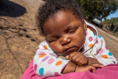 Cloeseup of African child two months sleeping in his mothers arms.のeditorial素材