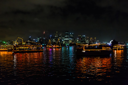 Reflecting boats in Sydney bay waiting for fireworks to celebrate the new year 2015, shot from a boat in a very windy and cloudy sky.  View of Opera House theater and city skyline from the sea.の写真素材