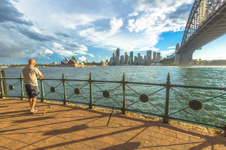 Sydney, Australia - December 29, 2014:Fisherman on the path under the Sydney Harbour Bridge. City skyline and Opera House behind.のeditorial素材