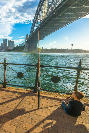 Sydney, Australia - December 29, 2014:Child fishing at sunset under the Sydney Harbour Bridge . City skyline behind.のeditorial素材