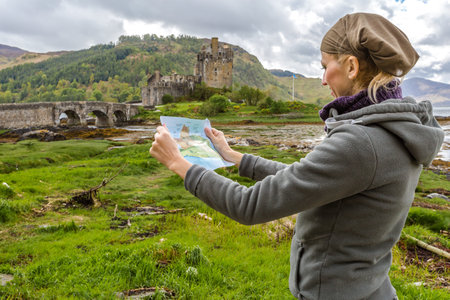 Young tourist looks at the brochure of Eilean Donan Castle situated on an island at the confluence...
