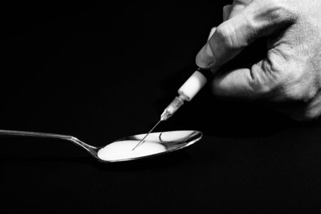 Closeup of hand holding a syringe that sucks dissolved heroin on a spoon, black background. Concept of drug abuse, lawlessness, danger, degradation, hopeless.の写真素材