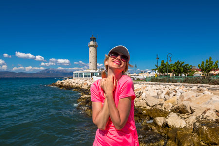 A young, smiling, fashionable woman posing in front of Patras lighthouse, Peloponnese, Greece. The...