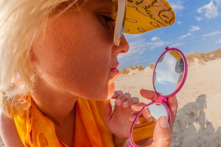 Closeup of young woman looks in the mirror to check her makeup on the beach. Fisheye lens effect.の写真素材