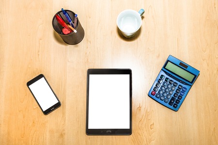 Flat lay of a business and finance desktop with tools: pad, calculator, penholder,coffee cup, and tablet on wooden table. Blank white screen for copy spaceの写真素材