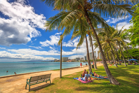 Waikiki ,Oahu, HI - August 27, 2016: people take the sun lying on the lawn fronting the popular Queen's Beach section of Waikiki Beach. Wooden benches on Queens Beach boardwalk.のeditorial素材