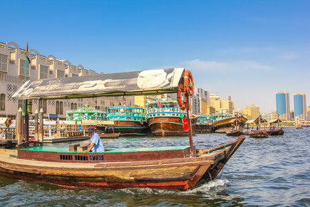 Dubai, United Arab Emirates - May 3, 2013: close up of traditional wooden boat docked on the Bay Creek in United Arab Emirates. On background, skyline of Deira, the old downtown of Dubai.のeditorial素材