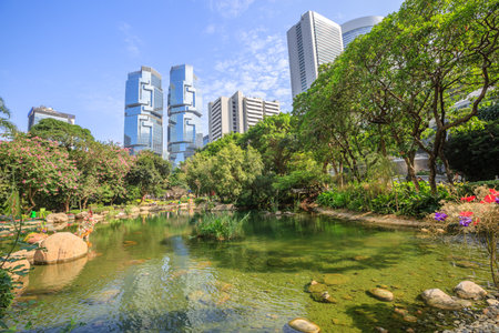 Beautiful view of pond at the lush Hong Kong Park surrounded by skyscrapers in the Central business district in Hong Kong island. Sunny day with blue sky.のeditorial素材