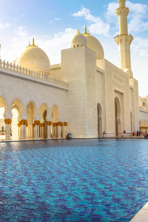 Abu Dhabi, United Arab Emirates - April 22, 2013: front and entrance of Sheikh Zayed Grand Mosque, the largest mosque in the UAE. Details of one of the pools along the arcades with columns. Shot at sunsetのeditorial素材