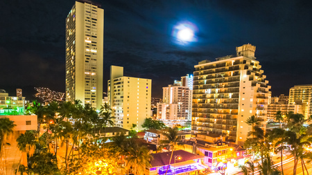 Moonlight aerial view on night traffic of Waikiki city in Oahu, Hawaii, United States. Moving people, car glowing trails in the street. City night lights of shops, shining full moon. Nightlife conceptの写真素材