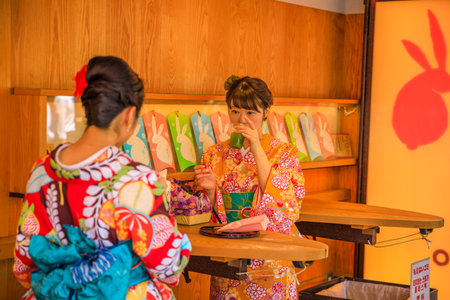 Tokyo, Japan - April 19, 2017: two young women in traditional japanese kimonos drink Amazake inside a famous stand selling Kibi-dango on Nakamise-dori street at Senso-ji Temple, Asakusa.のeditorial素材