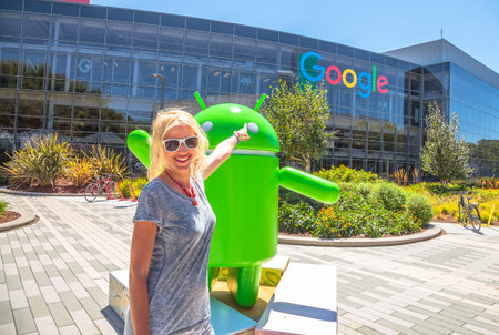 Mountain View, California, USA - August 15, 2016: Smiling woman showing Google sign on facade of Google Headquarters building. Young tourist visiting popular technology company in Silicon Valley.のeditorial素材