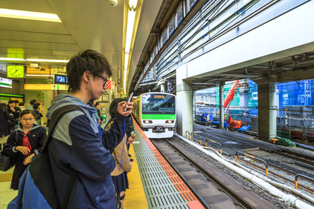 Tokyo, Japan - April 17, 2017: a boy looks at his smarth phone while waiting the Yamanote Line, the most important train line in Tokyo. The Yamanote is a JR line and a circular ring around city centerのeditorial素材