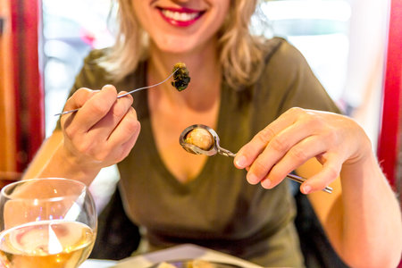 Smiling woman eating snails with herbs butter. Traditional French dish. Female enjoying in typical...