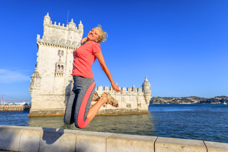 Happy blonde caucasian woman jumping at Belem Tower,in Belem District, Tagus River. Lifestyle traveler female enjoying Torre de Belem. Freedom and travel conceptの写真素材