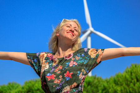 Portrait of blonde woman with open arms enjoying for modern power technology of wind turbines....