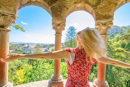 Carefree blonde caucasian woman with open arms looking Sintra panorama. Female tourist enjoying in a sunny day.の写真素材