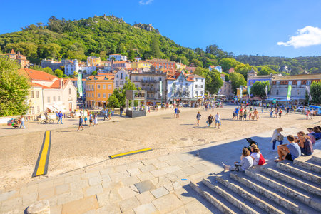 Sintra, Portugal - August 8, 2017: Tourists sitting on steps of National Palace of Sintra in the popular main Amelia Square with Castle of the Moors on background. Sintra urban center in a sunny day.のeditorial素材
