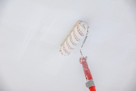 Paint stick roller painting a blank ceiling, in empty white room with copy space.の写真素材