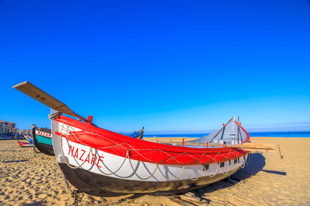Nazare, Portugal - August 16, 2017: colorful traditional old wooden fishing boats on the beach of fishing village of Nazare. The fishing tradition in Nazare, Nazare boats exhibition.のeditorial素材