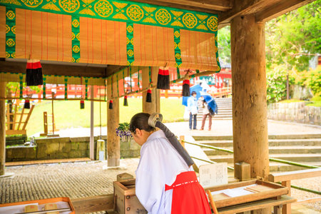 Nara, Japan - April 26, 2017: back of Shinto Miko, a maiden or a supplementary priestess inside main sanctuary of Kasuga Taisha in Nara. The mikos attire consists of a white haori and a red hakama.のeditorial素材