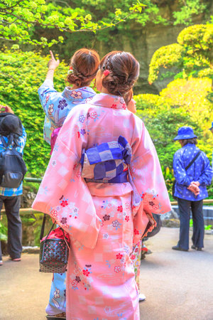 Kamakura, Japan - April 23, 2017: Vertical shot of back of Japanese women in zen garden, dressed in classic pink kimonos at Takera Hokoku-ji Temple of Kamakura. Looking beauty of nature.のeditorial素材