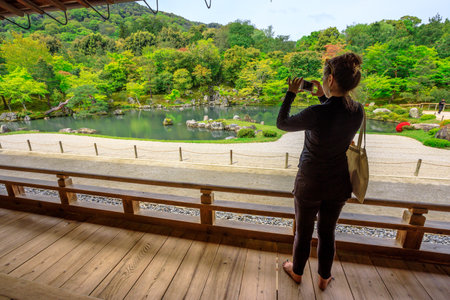 Kyoto, Japan - April 27, 2017: japanese woman from Hojo Hall photographs Sogen Garden around Sogen-chi Pond in Tenryu-ji Zen Temple in Arashiyama. Springtime.のeditorial素材