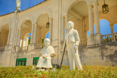Fatima, Portugal - August 15, 2017: statues of Francisco and Jacinta, the little shepherds who saw the apparitions of Virgin Mary. The colonnade of Sanctuary of Our Lady of Fatima on the background.のeditorial素材