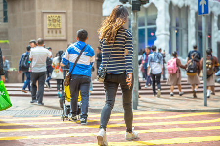 Hong Kong, China - December 6, 2016: Asian girl walking with her mobile phone in hand along the intersection of Times Square, largest shopping mall in Causeway Bay, the luxury shopping district.のeditorial素材
