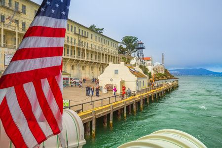 San Francisco, California, United States - August 14, 2016: Alcatraz penitentiary sally port with main building with guard tower. Dock full of tourists waiting for boat. American flag waving.のeditorial素材