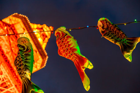 Tokyo, Japan - April 23, 2017: details of Koinobori a carp-shaped wind socks traditionally flown in Japan to celebrate Childrens Day. Blurred Tokyo Tower by night on background. Horizontal shot.のeditorial素材