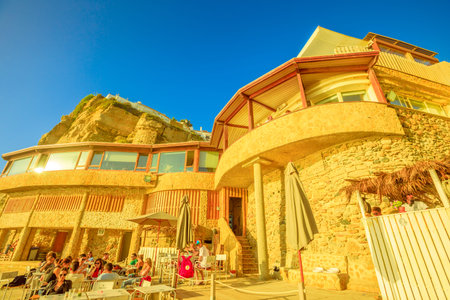 Azenhas do Mar, Portugal - August 5, 2017: bottom view of restaurant and high cliff of ex fishing village of Azenhas do Mar in Colares on the Atlantic Coast, seen from the beach. Sunset light.のeditorial素材