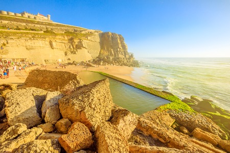 Scenic promontory and beach at sunlight of Azenhas do Mar with famous natural pool visible at low tide on Atlantic Ocean in Portugal. Popular Portuguese seaside resort near Colares and Sintra.の写真素材