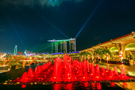 Singapore - April 28, 2018: Fullerton Fountain color red near to Fullerton Bay Hotel in Clifford Square, Marina Bay walkway promenade. Marina Bay Sands during Laser show at night on background.のeditorial素材