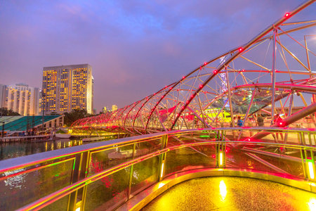Modern architecture of pedestrian bridge illuminated at blue hour on the foreground in Marina Bay Area, Singapore city. Famous place for travel destination. Scenic cityscape at twilight.のeditorial素材