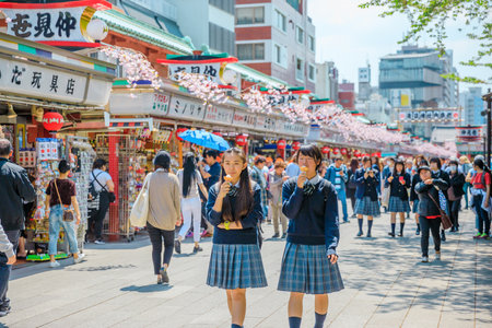 Tokyo, Japan - April 19, 2017: young teens in school uniforms walking on Nakamise Dori, street with food and souvenirs shops, eating an ice cream. Kaminarimon Gate of Sensoji Temple on background.のeditorial素材