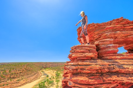 Backpaker woman over iconic Natures Window, with rocks rippled with red and white banded, pointing Murchison River in Kalbarri National Park, Western Australia. Australia, outback travel. Copy space.の写真素材