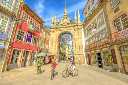 Braga, Portugal - August 12, 2017: children cycling in front of popular Arco da Porta Nova. Arch of New Gate in Baroque style is part of Braga city walls and is one of the oldest cities in Portugal.のeditorial素材