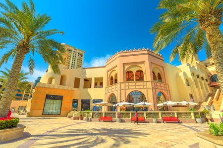 Doha, Qatar - February 18, 2019:Benches and palm trees along marina walkway promenade in Porto Arabia at the Pearl-Qatar, Doha. Persian Gulf in Middle East. Sunny day with blue sky.のeditorial素材
