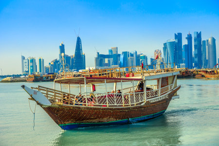 Doha, Qatar - February 23, 2019: people tourists on dhow and seafront of Doha West Bay skyline with...
