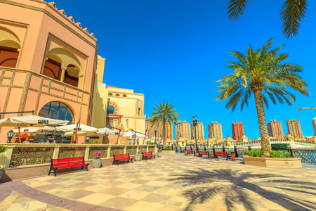 Doha, Qatar - February 18, 2019: benches and palm trees along marina walkway promenade in Porto...