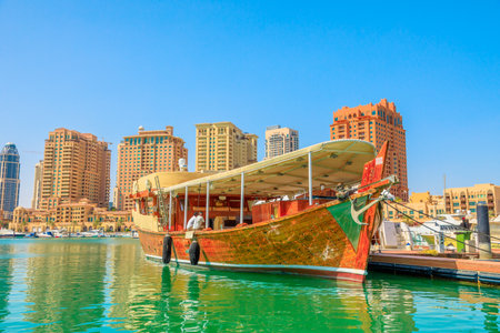 Doha, Qatar - February 18, 2019: traditional wooden boats docked in Porto Arabia at the Pearl-Qatar with residential buildings on background. Persian Gulf in Middle East. Sunny blue sky.のeditorial素材