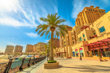 Doha, Qatar - February 18, 2019:Palm trees along luxury marina corniche walkway promenade in Porto...